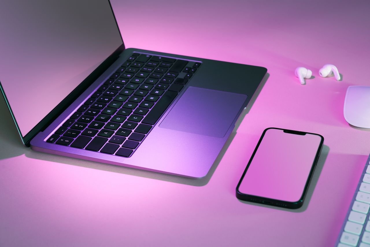 Mastering the First Impression: Your intriguing post title goes here Stylish tech workspace featuring a laptop, smartphone, and earphones under pink lighting.