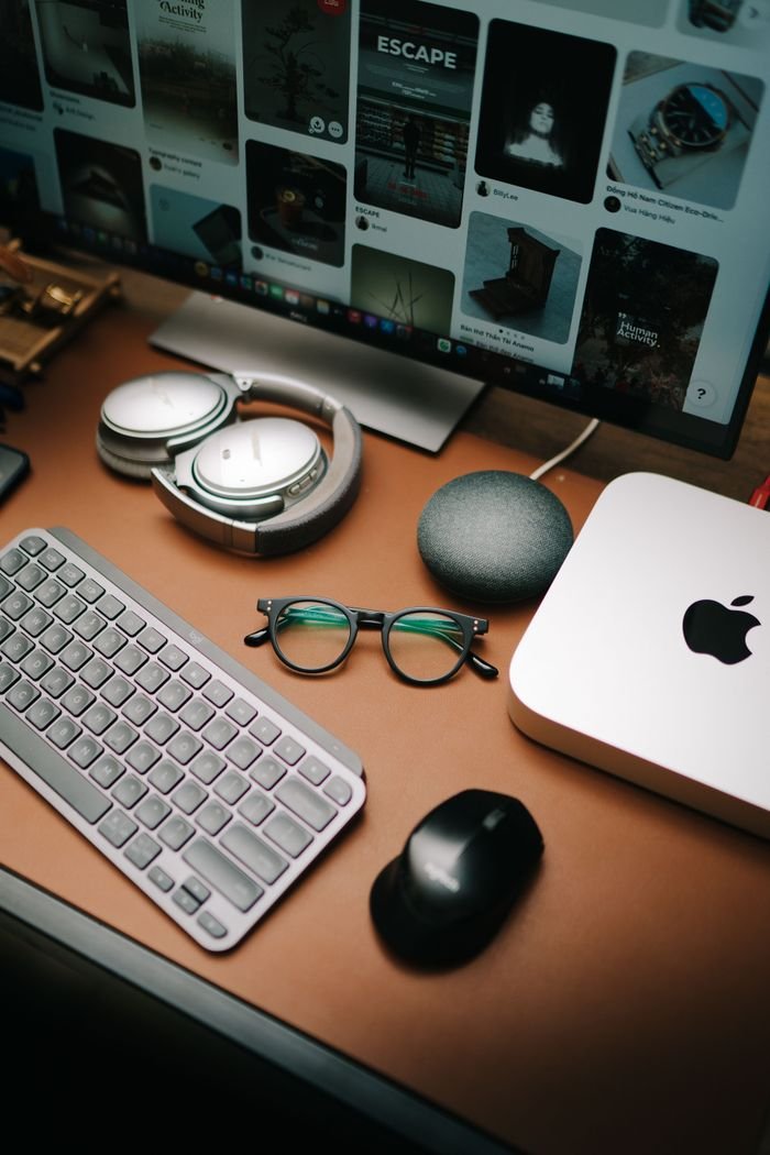 A stylish workspace featuring a keyboard, mouse, eyeglasses, headphones, and a screen displaying digital content.